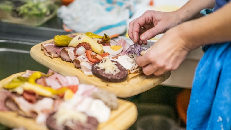 Brettljause, © Fam. Rieder Person prepares a snack with sausage, cheese and vegetables.