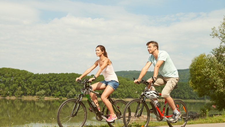 nibelungengau-rad-c-klaus-engelmayer, © Klaus Engelmayer Two people riding bicycles along a river in sunny weather.