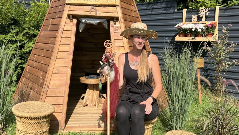 Natural history witch garden Angela, © Angela Dangl Woman in a straw hat sits in front of a wooden tepee in the garden.