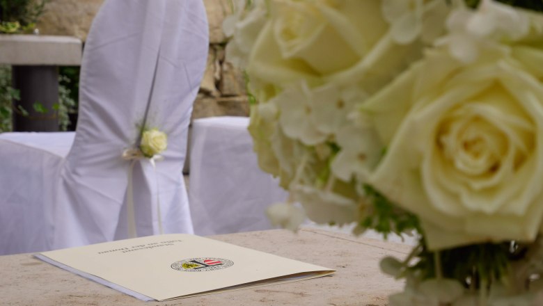 Wedding in the love garden, DIE GARTEN TULLN, © DIE GARTEN TULLN Close-up of a wedding decoration with white roses and a document on a table.