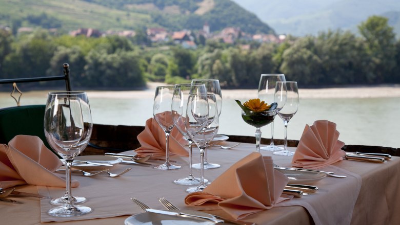 Restaurant terrace, © Fally Set table on a restaurant terrace with a view of a river and wooded hills in the background.