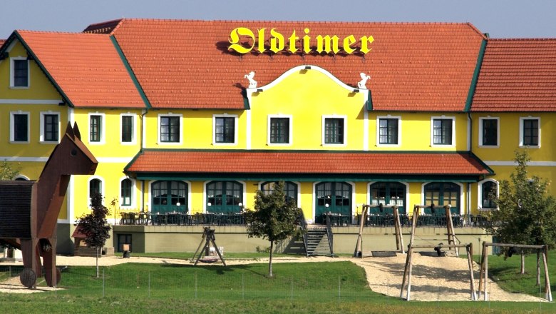 Guntramsdorf, © Autobahnrestaurant Oldtimer Yellow building with a red roof and the inscription 'Oldtimer', next to it a playground with a large wooden figure.