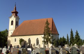 Exterior view of the church, © Johann Merl / Pfarrkirche Ebreichsdorf Exterior view of a church with a cemetery in the foreground and a blue sky.