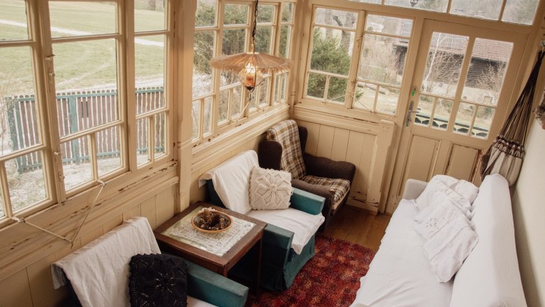 Orlet on the Rax, © Sofia Orlet Cozy winter garden with armchairs, sofa and table, surrounded by large windows with a view of the outside.