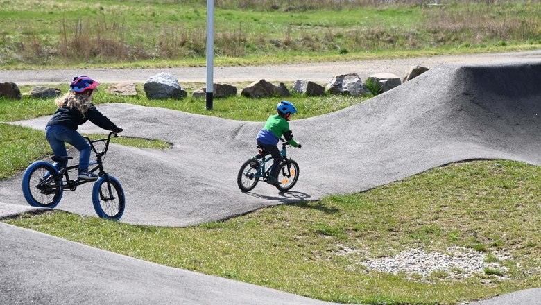 Pump track, © Markus Berger Two children riding bikes on an outdoor pump track.