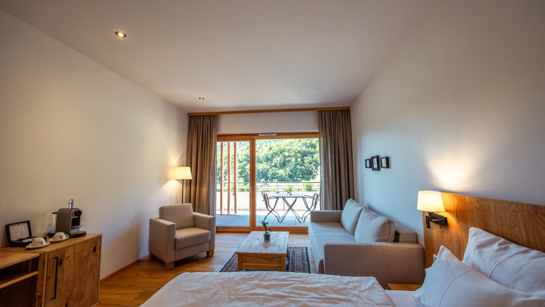 Wine Hotel Nigl, © Niederösterreich Werbung / Maximilian Pawlikowsky Modern hotel room with bed, sofa, armchair and balcony with a view of the countryside.