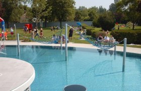 Aqua Splash" adventure pool, © Erlebnisbad "Aqua Splash" An outdoor pool with hammocks over the water and people in the background on the sunbathing lawn.