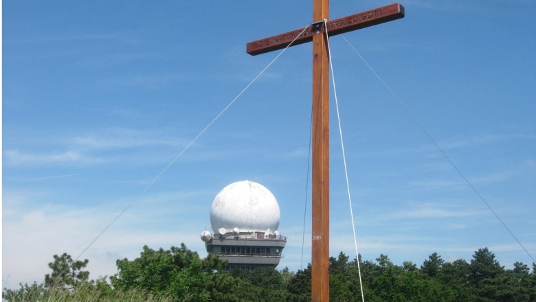 Bush hill, © Gemeinde Niederleis A wooden cross in front of a radar dome on the Buschberg, surrounded by trees and blue sky.