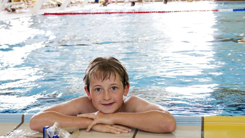 badearena_hallenbad_c_stadt-krems_barbara-elser-3, © Stadt Krems_c_Barbara Elser A boy is leaning against the edge of an indoor pool, smiling and wearing swimming goggles.