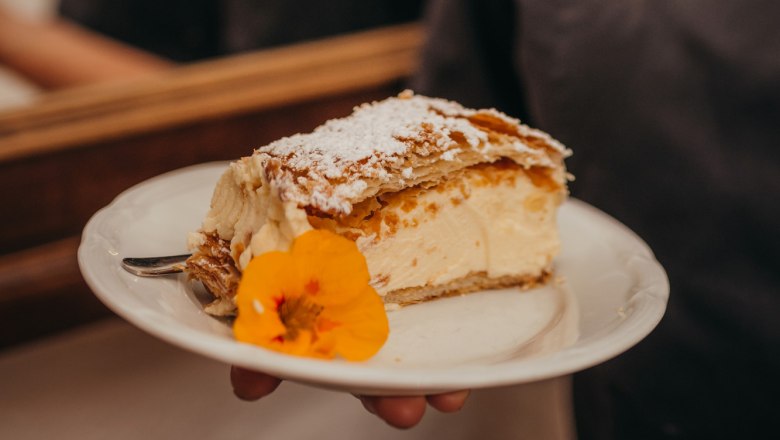 Homemade pastries, © Niederösterreich Werbung/Daniela Führer One person is holding a plate with a piece of cake decorated with a flower.