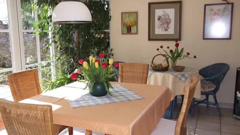 Guesthouse am Steindl, © Gästehaus am Steindl A cozy dining area with a table holding a bouquet of flowers, surrounded by wicker chairs and decorative pictures on the wall.