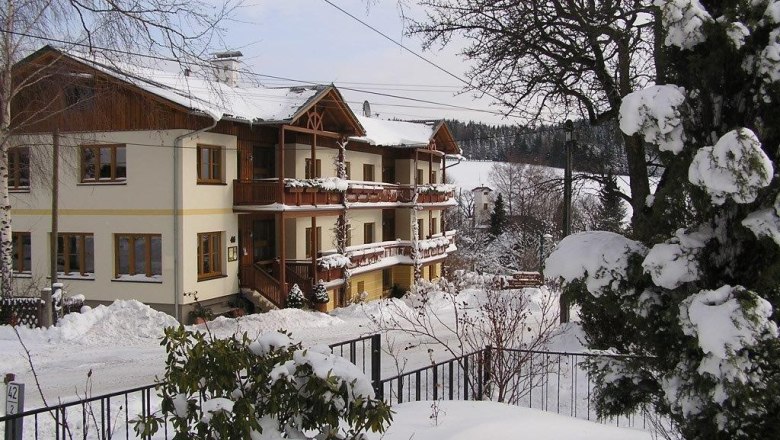 Ofnerhof St. Corona am Wechsel, © familie-gruber A snow-covered building with wooden balconies in a wintry landscape.