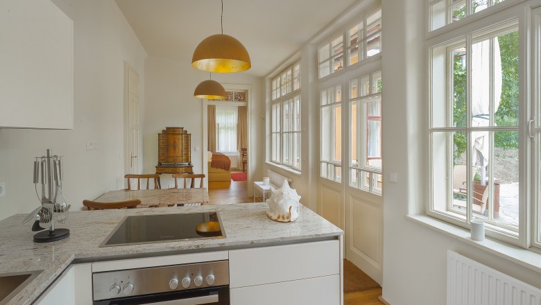 Living room of Suite Emma at Guntrams Estate, © Hubert Dimko/ Harald-Krischanz Interior view of a modern kitchen with large windows, a stove and a dining table.