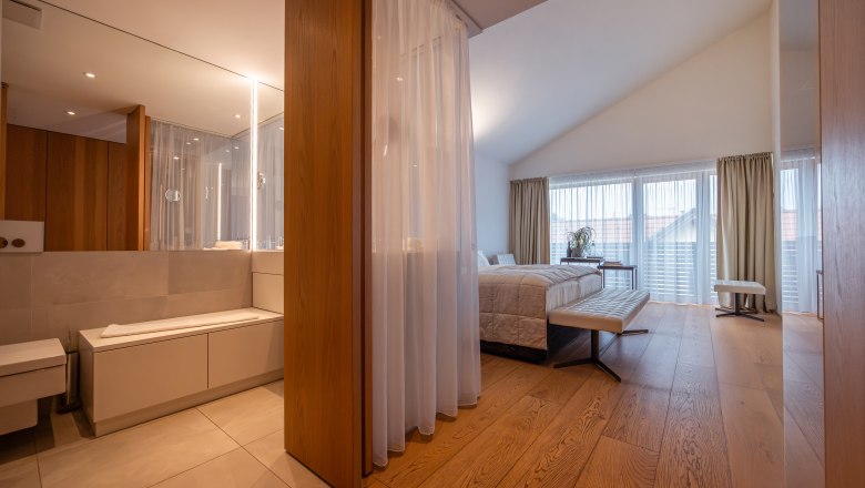 Relais & Chateaux Mörwald Hotel am Wagram, © Niederösterreich Werbung / Maximilian Pawlikowsky Modern hotel room with wooden floor, large bed and bathroom with mirror.