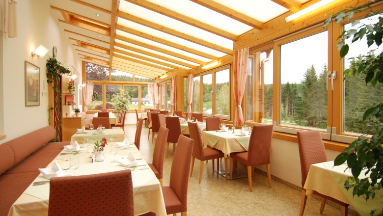 Inn - Pension Nordwald, © Gasthof - Pension Nordwald A bright conservatory of a restaurant with set tables and a view of a forest.