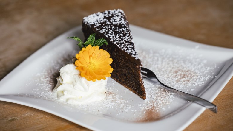 House cakes with whipped cream, © Niederösterreich Werbung/David Schreiber A piece of chocolate cake with powdered sugar, cream and a yellow flower on a plate.