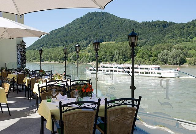 Terrace, © Residenz Wachau Terrace with covered tables, view of the river and passing ship, surrounded by green hills.