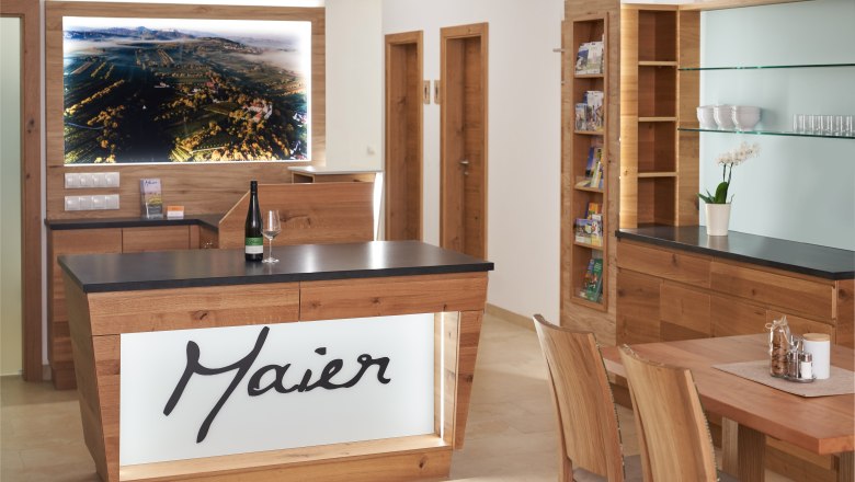 Weinhof Maier, © Weinhof Maier Interior view of a modern reception area with wooden furniture and a large landscape painting on the wall.