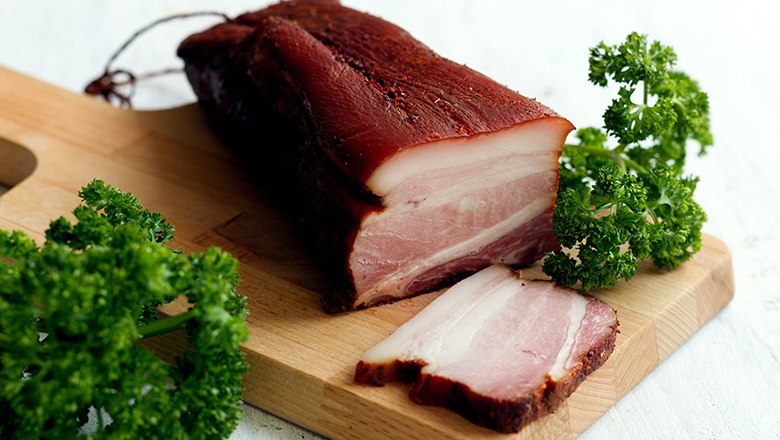 Bacon, © Sooo gut schmeckt die Bucklige Welt/ Viktoria Kornfeld A piece of bacon on a wooden board with parsley.