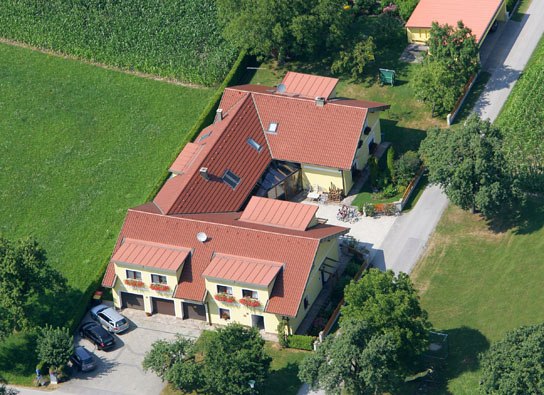 Vacation apartments & private rooms Leeb, © Privatzimmer Leeb Aerial view of a large house with red roofs, surrounded by green fields and trees.