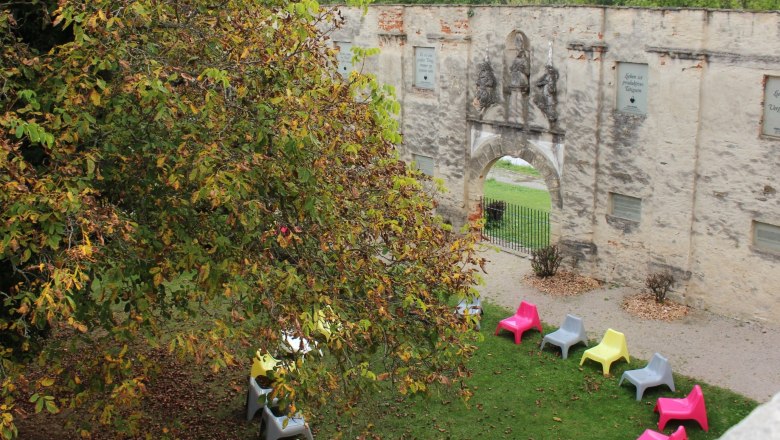 Pernegg Monastery, © © Zickbauer Natascha Colorful chairs in a circle on a meadow in front of an old stone wall with an archway.
