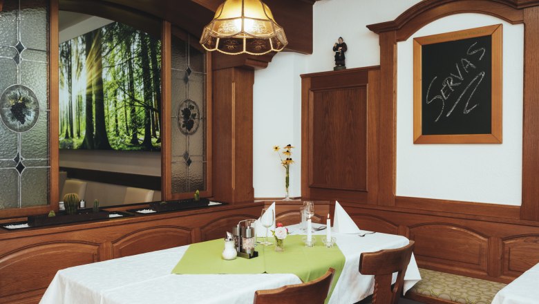 Parlor, Ballroom, Theme room, © Niederösterreich Werbung/David Schreiber Cozy guest room with wooden furniture, table with green tablecloth, candles and decoration. Window with forest motif and blackboard with 'Servas' lettering.