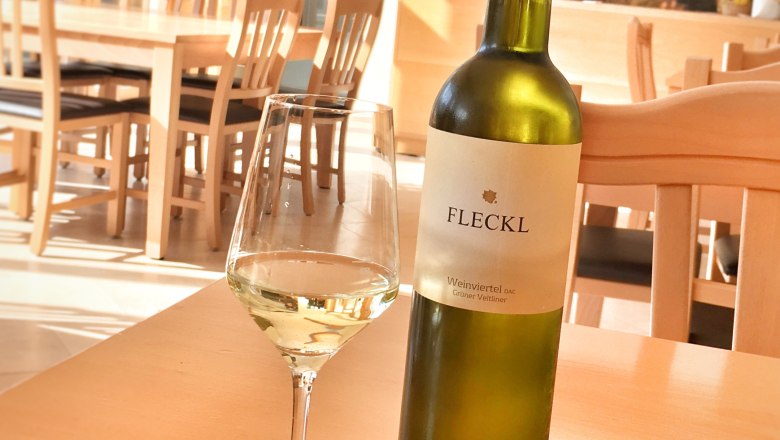 Tasting room, © Alexander Fleckl A bottle of white wine and a filled wine glass on a wooden table in a tasting room.