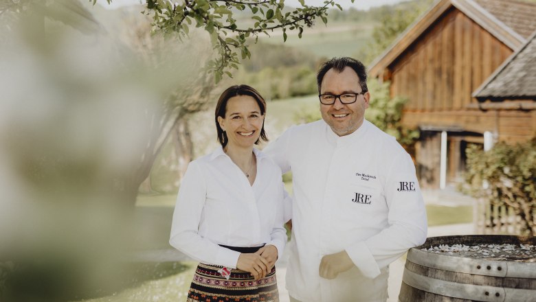 Veronika and Uwe Machreich, © Niederösterreich Werbung/Sophie Menegaldo A man and a woman stand smiling outside in front of a wooden building.