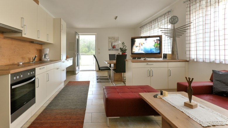 Eat-in kitchen, © Familie Harrauer Modern eat-in kitchen with fitted kitchen, dining table, TV and red seating furniture.