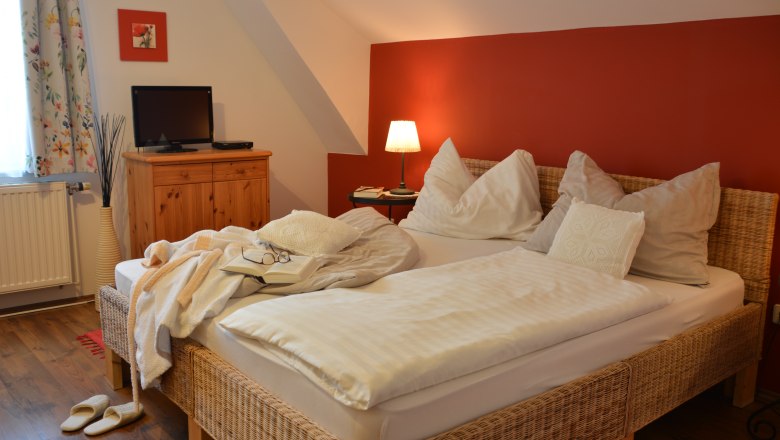 Double room, © Christine Nigl Cozy double room with red wall, bed, bedside lamp, TV and wooden furniture.