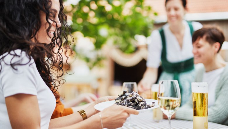 Mohnwirt Neuwiesinger, © © Waldviertel Tourismus, Gerhard Wasserbauer A woman serves a guest a poppy seed pasta in a beer garden while other guests sit at the table.