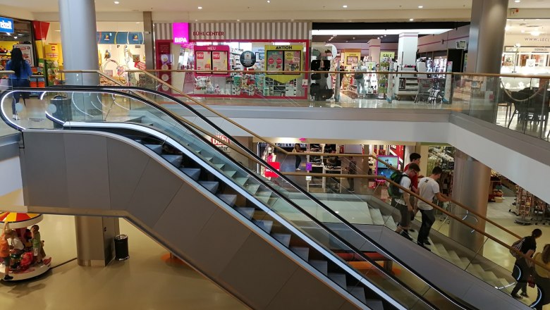 Bühl Center, © Roman Zöchlinger Interior view of a shopping center with escalators and stores.