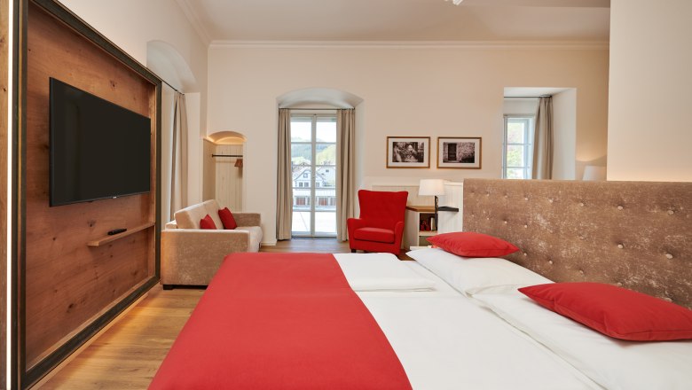 The castle on the Iron Road, © Dominik Stixenberger Hotel room with double bed, red bed linen, sofa, red armchair and large window.