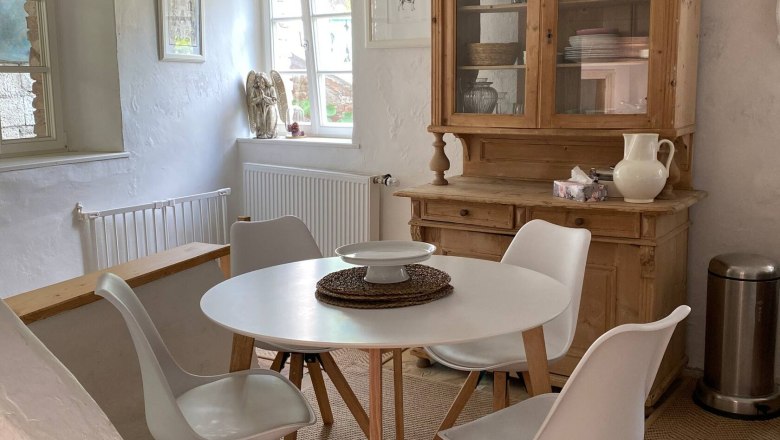 Dining area, © Familie Stagard Dining area with round table, four white chairs, wooden cupboard and decoration in a bright room.