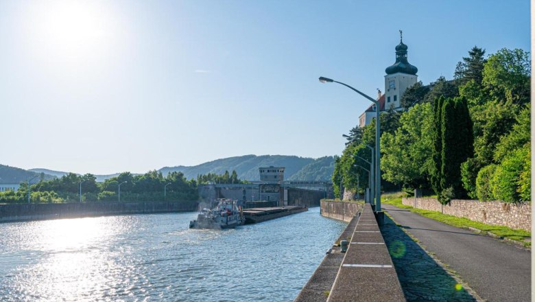 At the Donaulände, © Guestia GmbH River with ship and building on the bank, sunny sky.