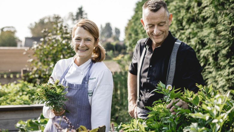 Landlady Alexandra Labenbacher-Konecny in the large pub garden, © Niederösterreich Werbung/David Schreiber Two people are standing in a garden, a woman in cooking clothes is holding herbs.