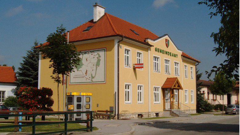 Municipal office, © Gemeinde Harmannsdorf-Rückersdorf A yellow building with the inscription 'Gemeindeamt', a coat of arms and a map on the wall.