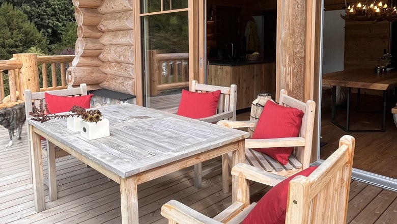 Terrace, © RaxChalet Wooden terrace with table and chairs, red cushions and a dog in the background.