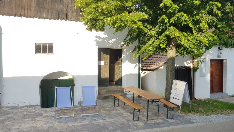 Cellar wellness area Alberndorf, © Gemeinde Alberndorf Two deckchairs and a table with benches in front of a white building with a tree.