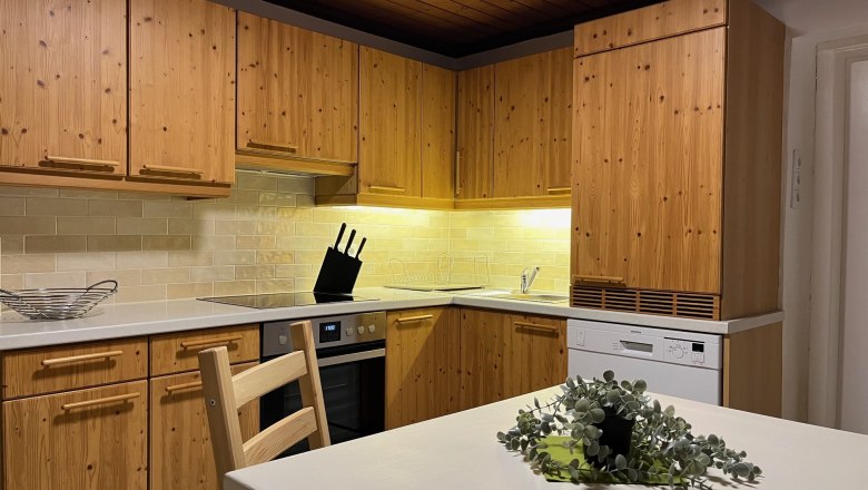 Kitchen, © Anita Gallei Kitchen with wooden furniture, stove, dishwasher and table with plant.