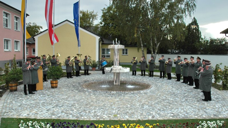 Enzersfeld, © Gemeinde Enzersfeld A brass band plays outside in front of a fountain, surrounded by flowers and flags.