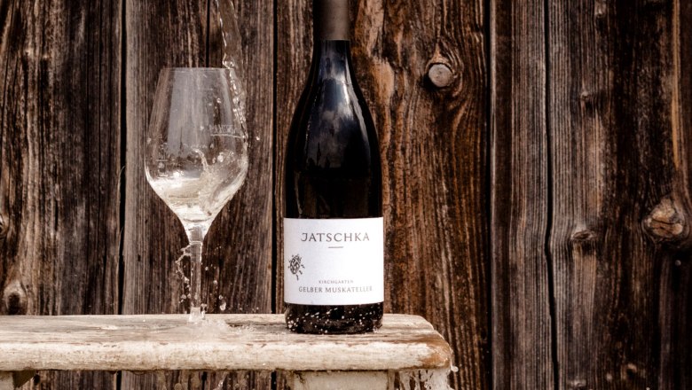 Winery Jatschka, © Astrid Bartl Wine bottle and glass with water in front of wooden wall.