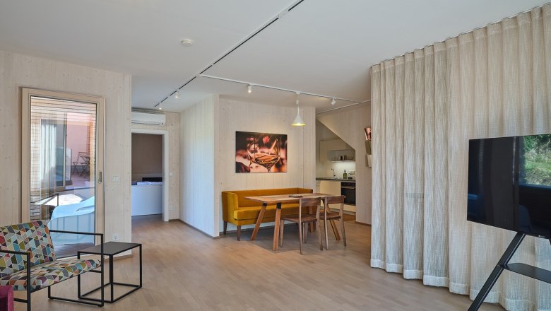 Equipment details in House Five, © Prof. Arch. DI Dietmar Kraus Modern living room with wooden floor, dining table, yellow bench, colorful armchair, large TV and open kitchen.