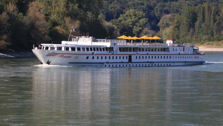 Danube boat on the doorstep, © Szilágyi A river cruise ship named Rossini sails on the Danube, surrounded by wooded banks.