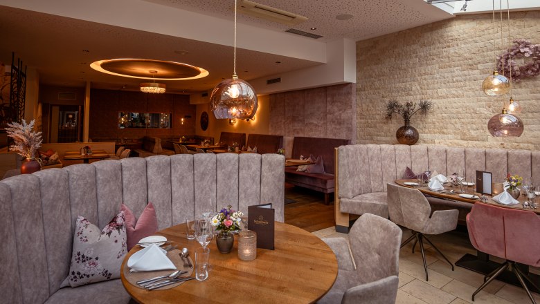 Hotel Schachner, © Niederösterreich Werbung / Maximilian Pawlikowsky Elegant restaurant with modern furnishings, round tables and upholstered benches under a glass roof.