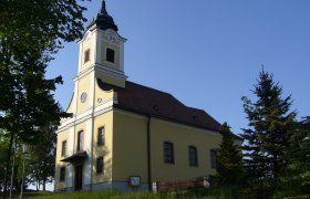 Haugschlag parish church, © Gemeinde Haugschlag Haugschlag parish church with yellow façade and tower, surrounded by trees.