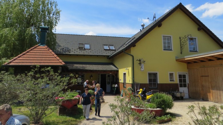 Gasthof Oase am Teich, © Urani A yellow inn with a gray roof and garden in the foreground.