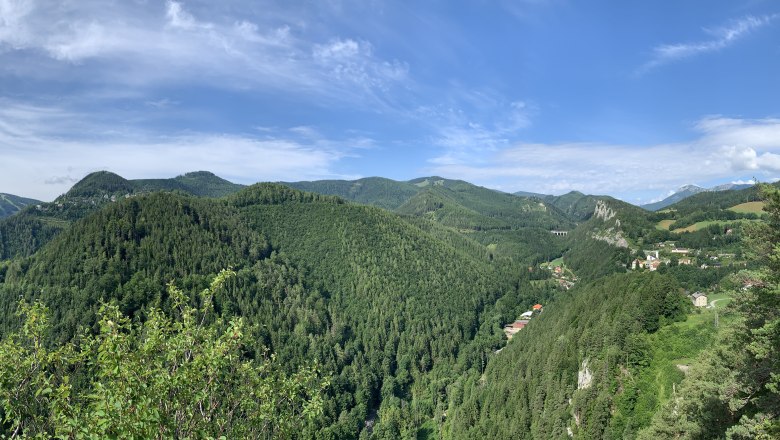 Breitenstein View Weinzettlwand, © Tourismusverband Semmering-Rax-Schneeberg Panoramic view of wooded hills and a valley with scattered houses under a blue sky.