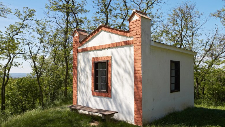 Hutberg Haugsdorf, © Initiative Pulkautal Small white building with red brick accents on a meadow surrounded by trees.