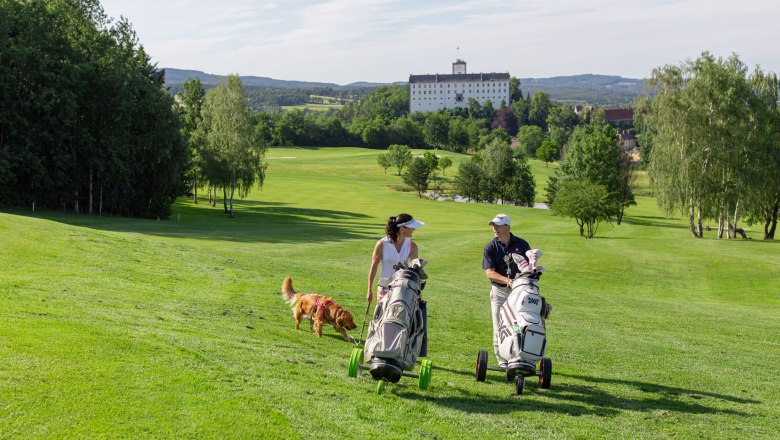 Weitra Golf Club, © www.michaelholzweber.com Two golfers with dog on a green golf course, castle in the background.